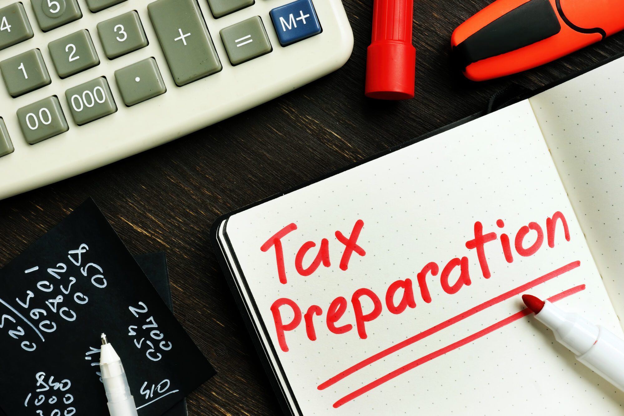 Desk with a calculator, pen, and notepad with the words "tax preparation" written on it