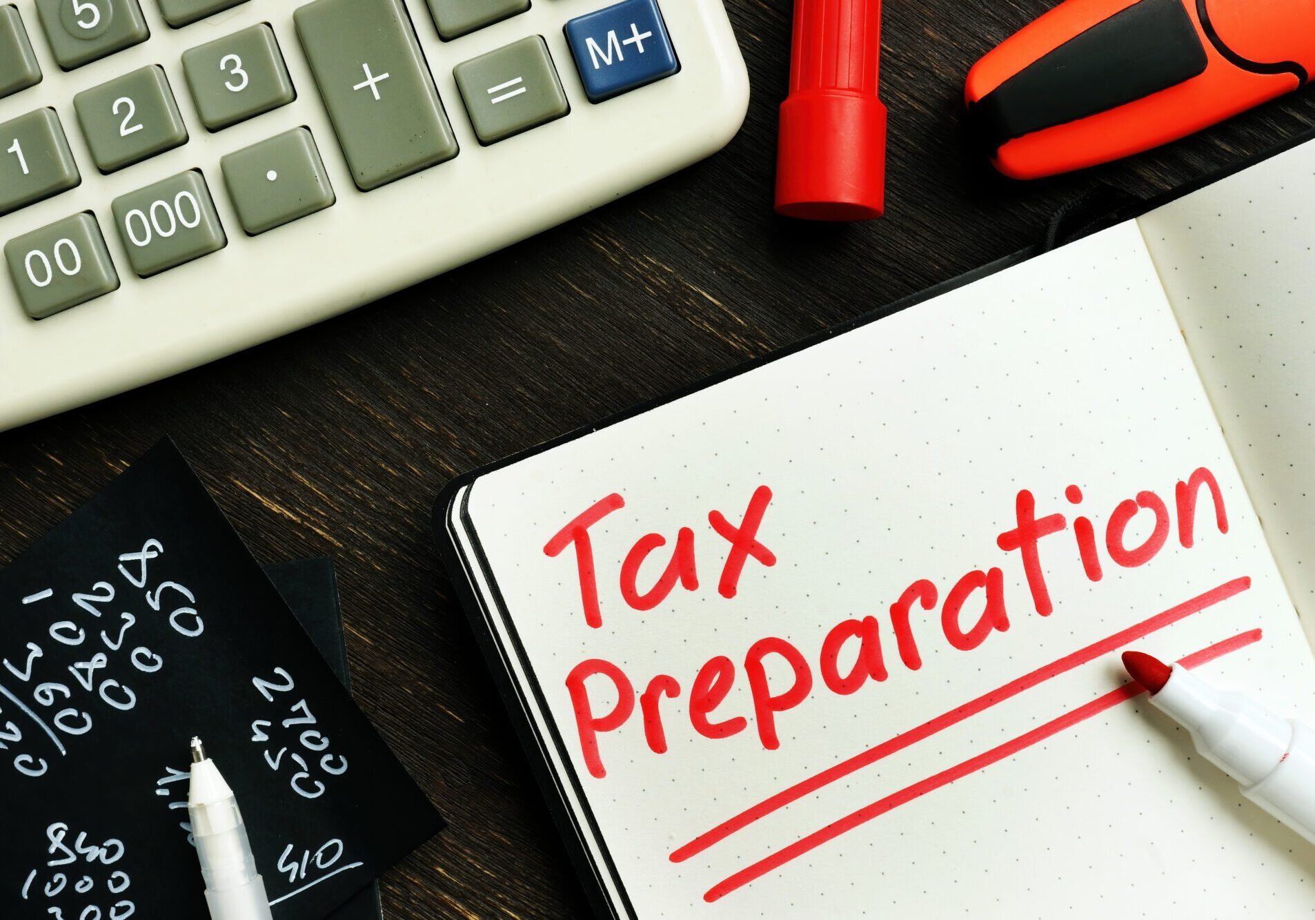 Desk with a calculator, pen, and notepad with the words "tax preparation" written on it